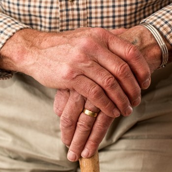 Hand of an elderly man standing and holding a walking stick
