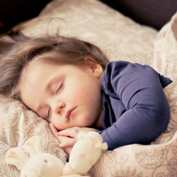 A toddler girl sleeping in her crib with a toy bunny